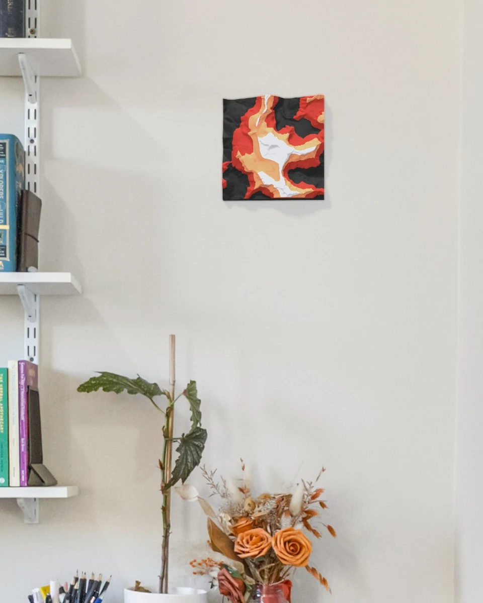 Mock-up in a real study: the Tititea / Mt Aspiring tile in Ember colours hung on its own on a pale wall beside white bookshelves, above a pot plant and dried flowers.